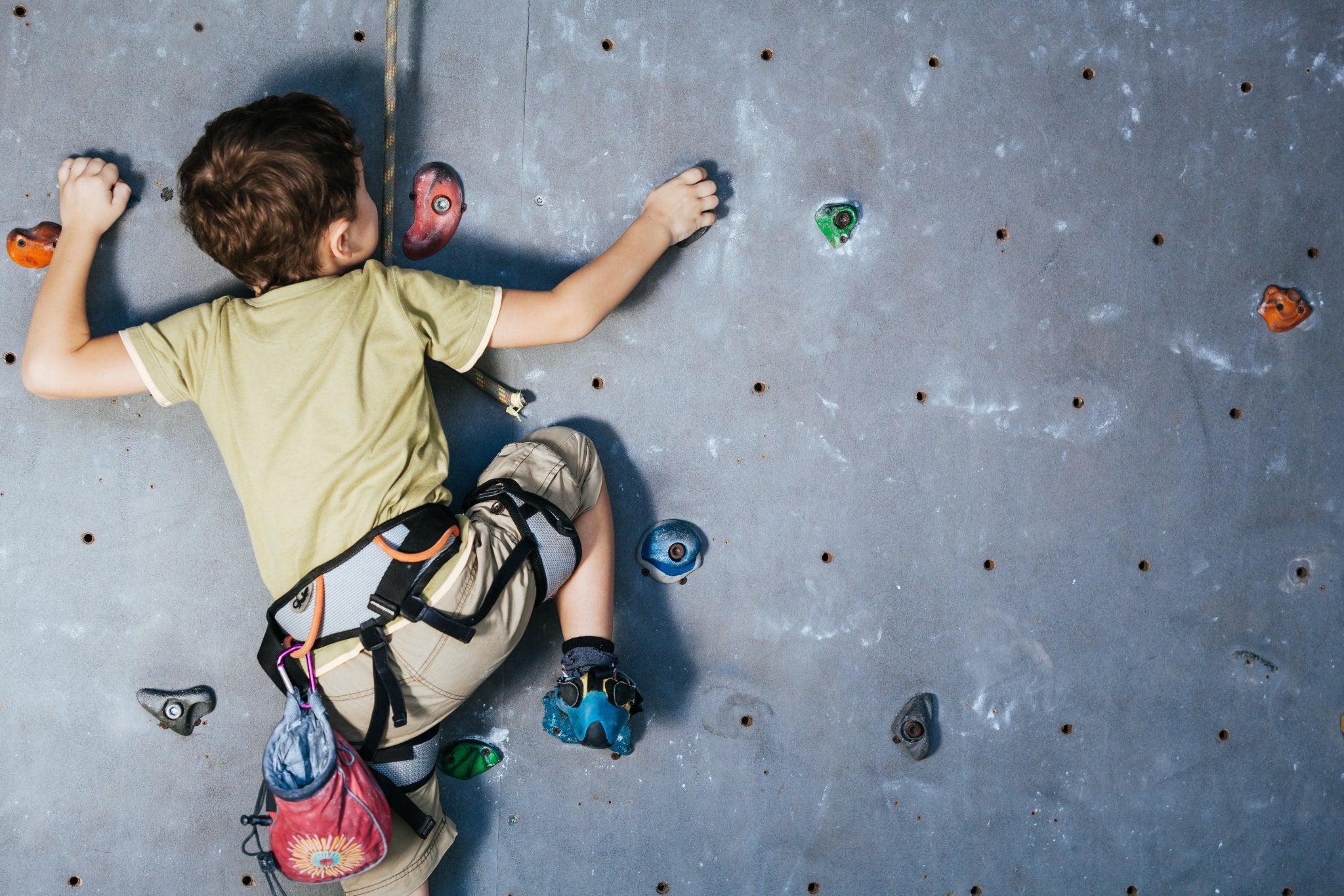 A little kid making his way up a rock-climbing wall.